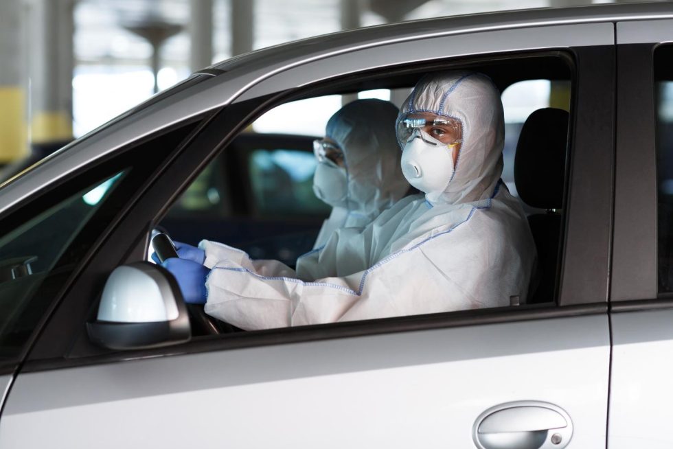 Quarantine time. People in coronavirus protective suits driving a car, pandemic concept